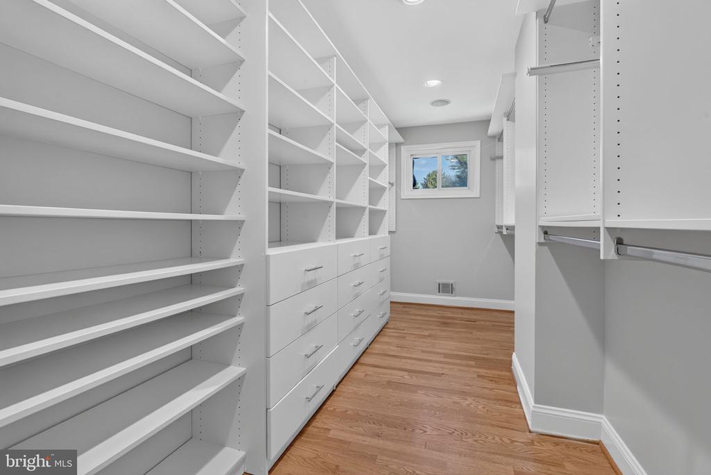 Walk-in closet with white built-in shelving and drawers, hardwood flooring, and a small window.