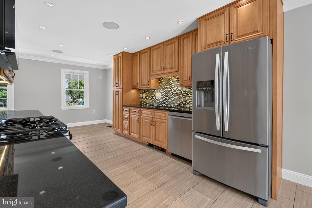 Kitchen with honey-toned cabinets, stainless steel appliances, black counters, and a mosaic tile backsplash.