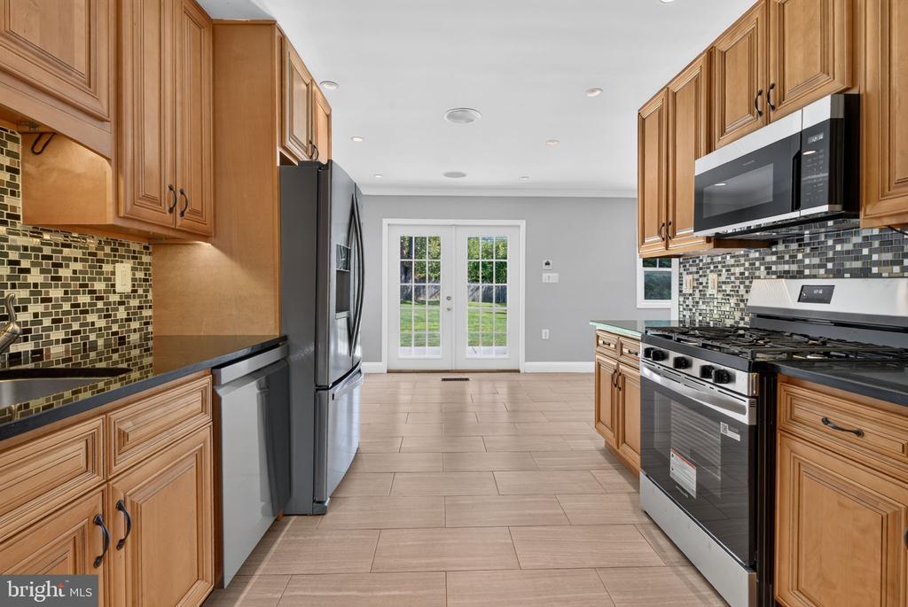 Kitchen with wood cabinetry, stainless steel appliances, mosaic backsplash, and French doors to the yard.