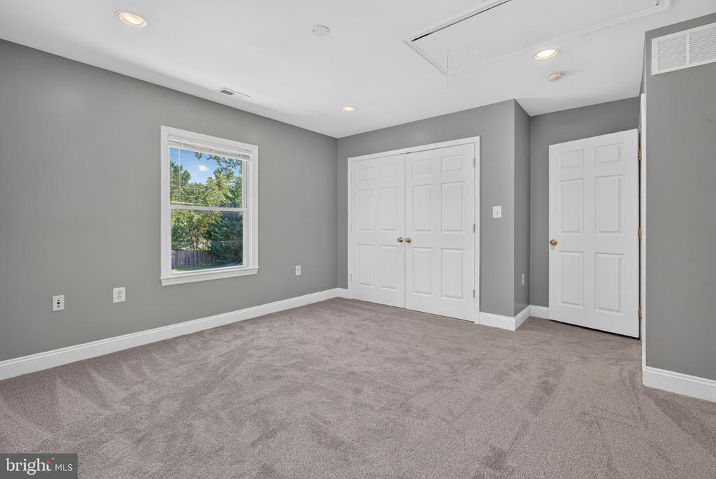 Empty bedroom with gray carpet, a window overlooking trees, and white closet doors.