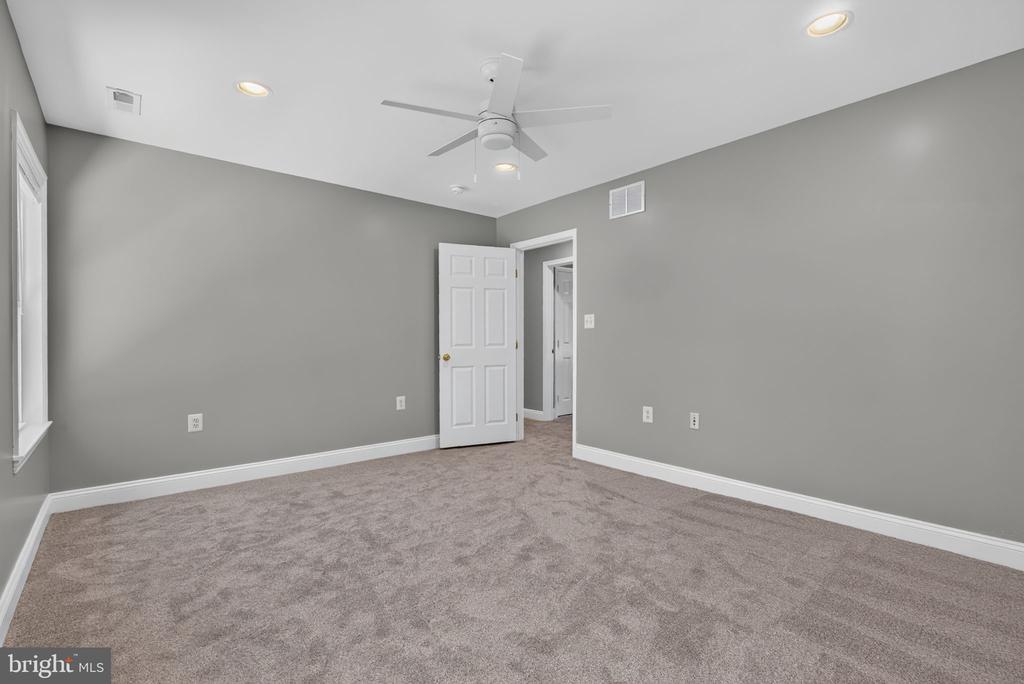 Unfurnished bedroom with gray walls, beige carpet, and a white ceiling fan.