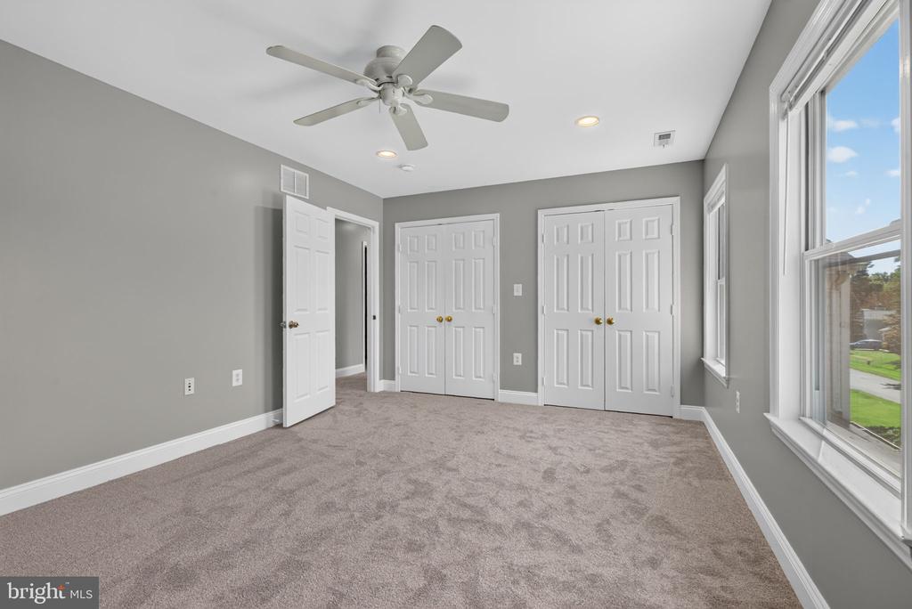 Vacant bedroom with beige carpet, a ceiling fan, double closets, and large windows.