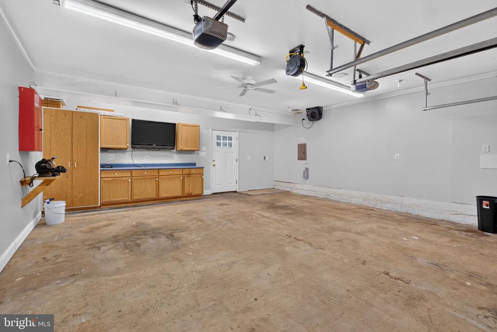 Garage with a bare concrete floor, overhead door tracks, and wooden cabinets and workbench.