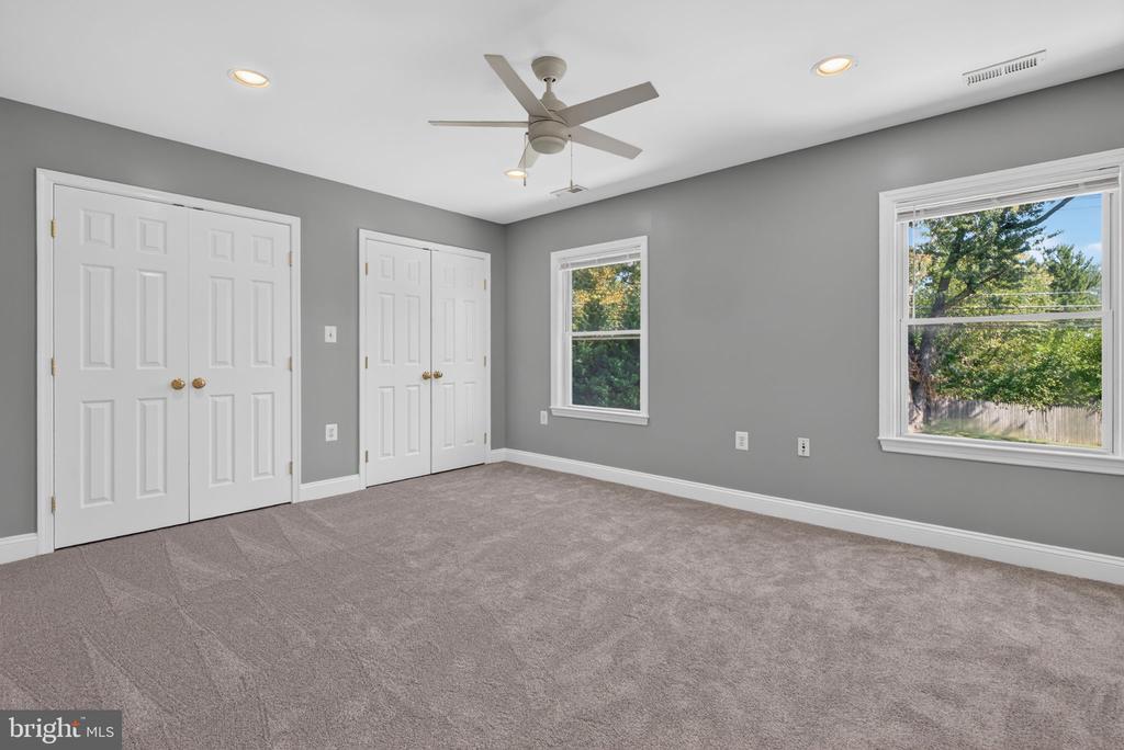 Empty bedroom with gray walls, taupe carpet, white closet doors, and a ceiling fan.