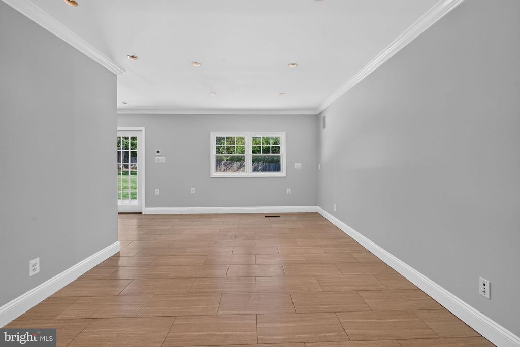 Vacant room with tan wood-look tile flooring, gray walls, and windows beside a glass-paneled door.