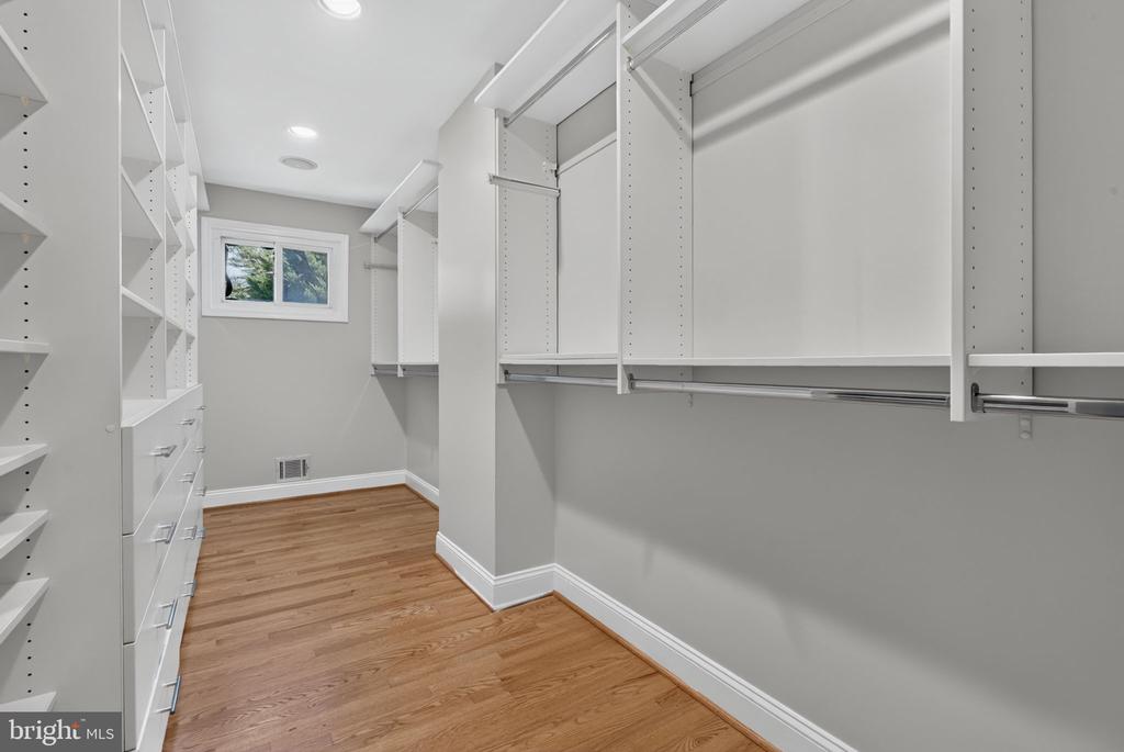 Walk-in closet with white built-in shelving, hanging rods, wood flooring, and a small window.