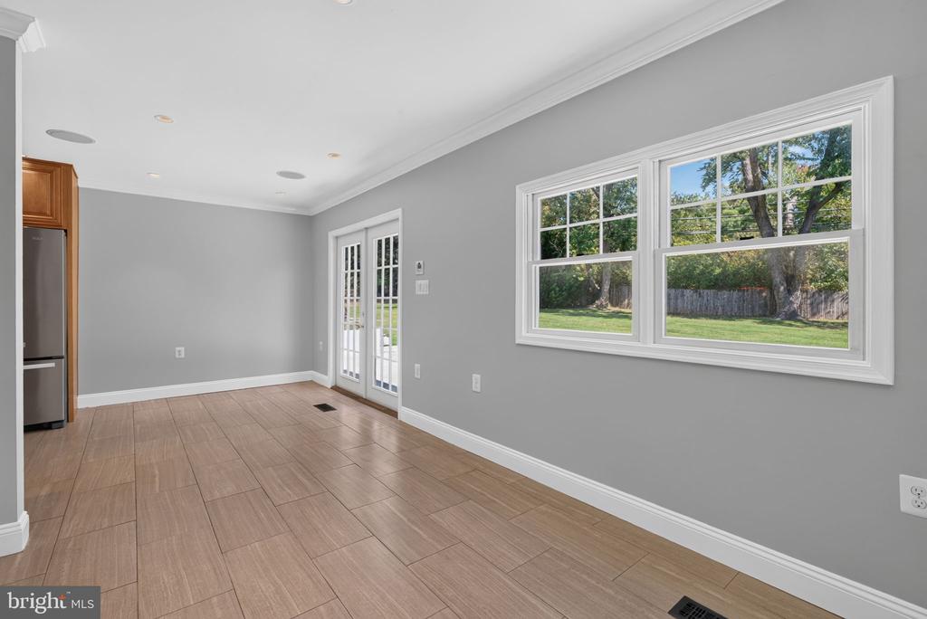 Empty dining area with tan tile flooring, French doors, and windows overlooking a fenced yard.