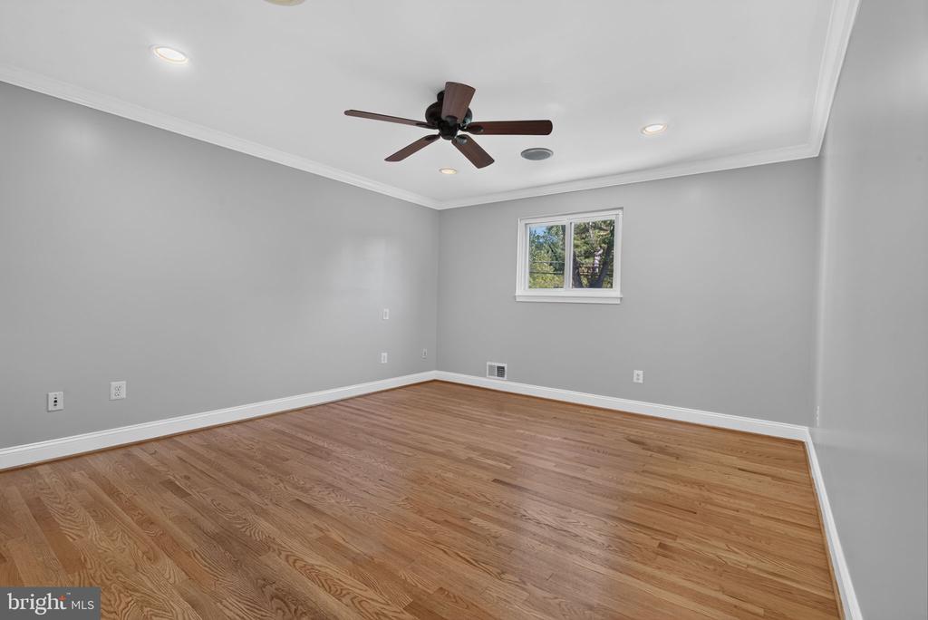 Vacant bedroom with hardwood floors, gray walls, a small window, and a dark ceiling fan.