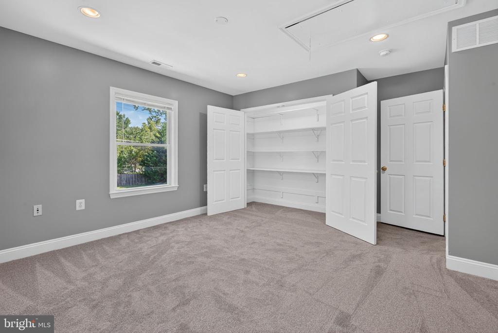 Empty carpeted bedroom with a large open, shelved closet and a window overlooking trees.