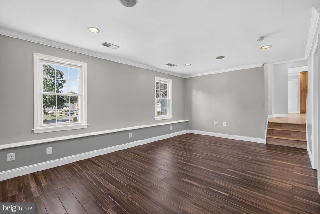 Empty living room with dark plank flooring, gray walls, and two windows.