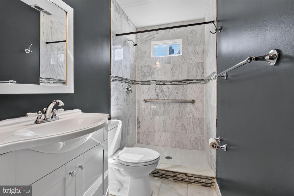 Bathroom with a marble-tiled walk-in shower, mosaic accent band, white vanity, and dark gray walls.