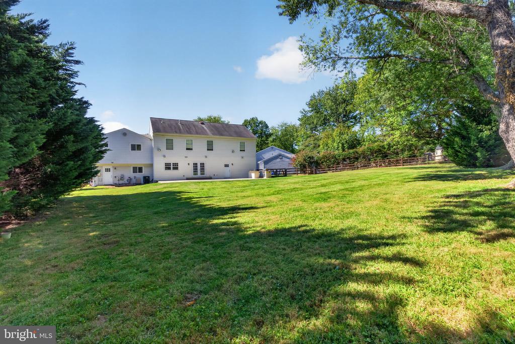 Rear of a white two-story house beyond a broad lawn, framed by mature trees.