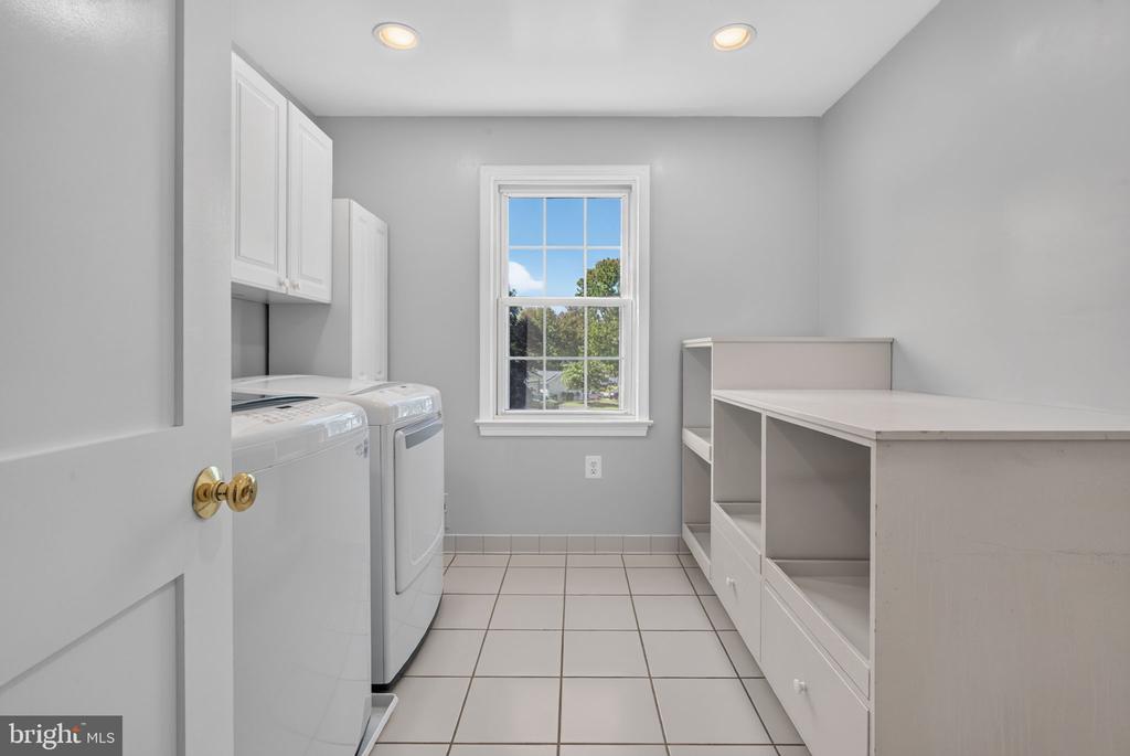 Laundry room with washer and dryer, white cabinetry, tiled floor, and a window overlooking trees.