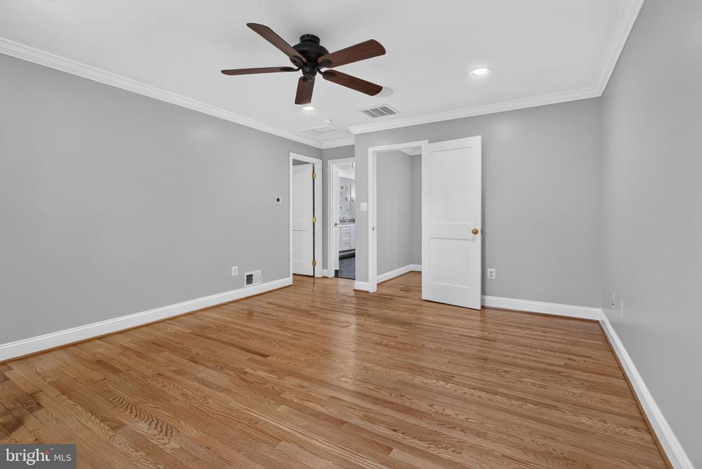Empty bedroom with hardwood floors, gray walls, and a dark wood ceiling fan.