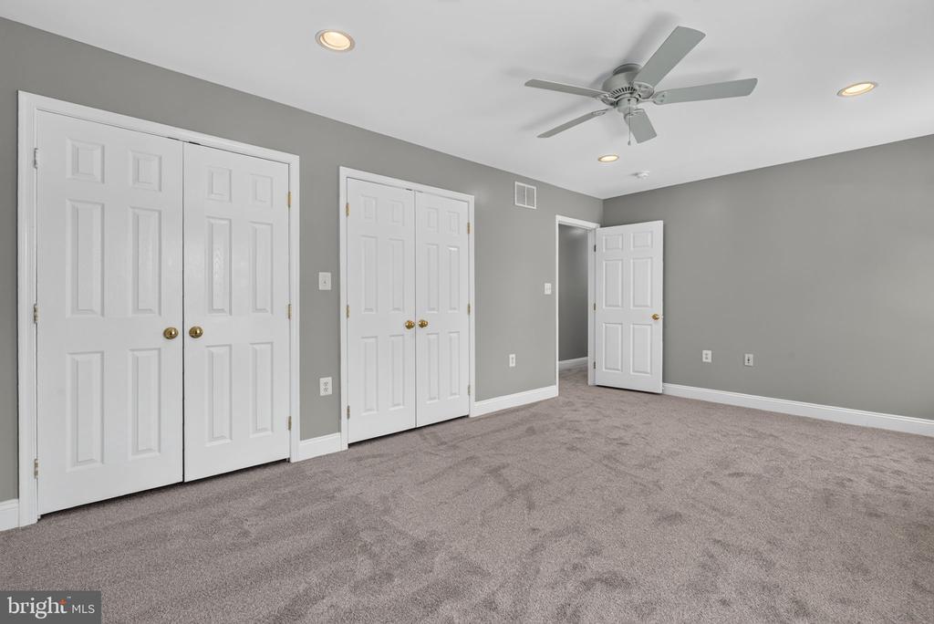 Empty bedroom with gray walls, double closets, a ceiling fan, and an open doorway.