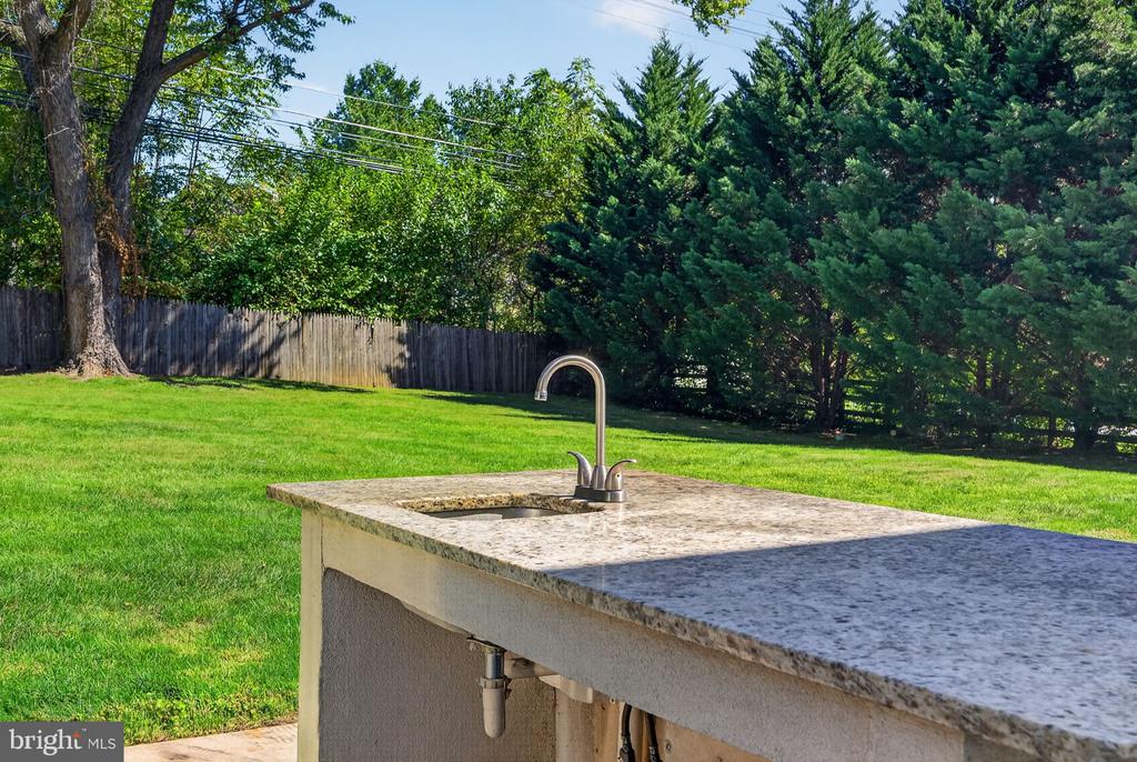 Outdoor sink and stone counter overlooking a fenced, tree-lined lawn.