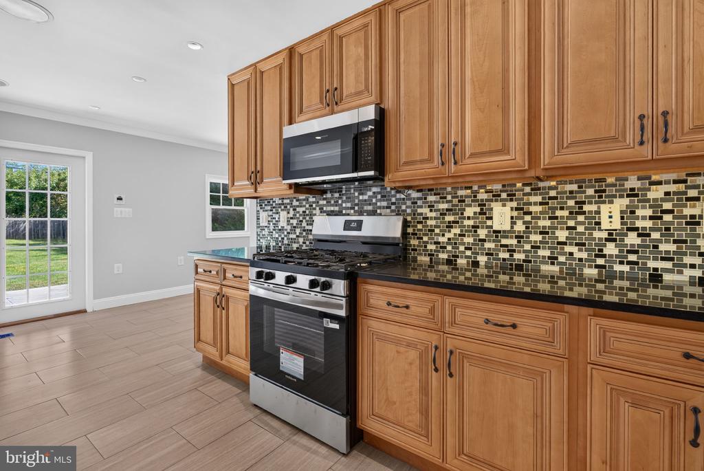 Kitchen with honey-colored cabinets, gas range, and mosaic tile backsplash.