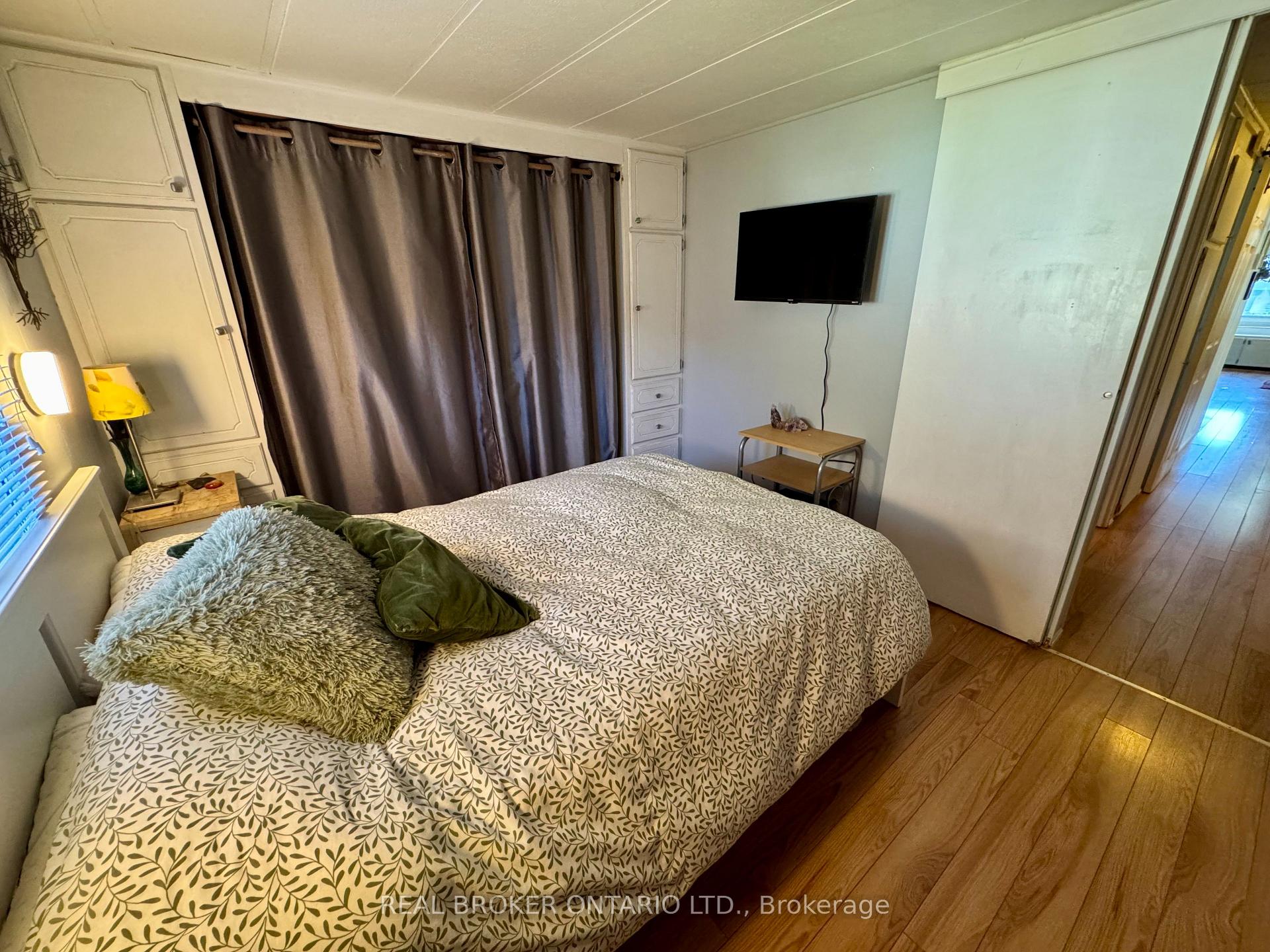 Bedroom with a patterned bedspread, layered pillows, and a wall-mounted television.