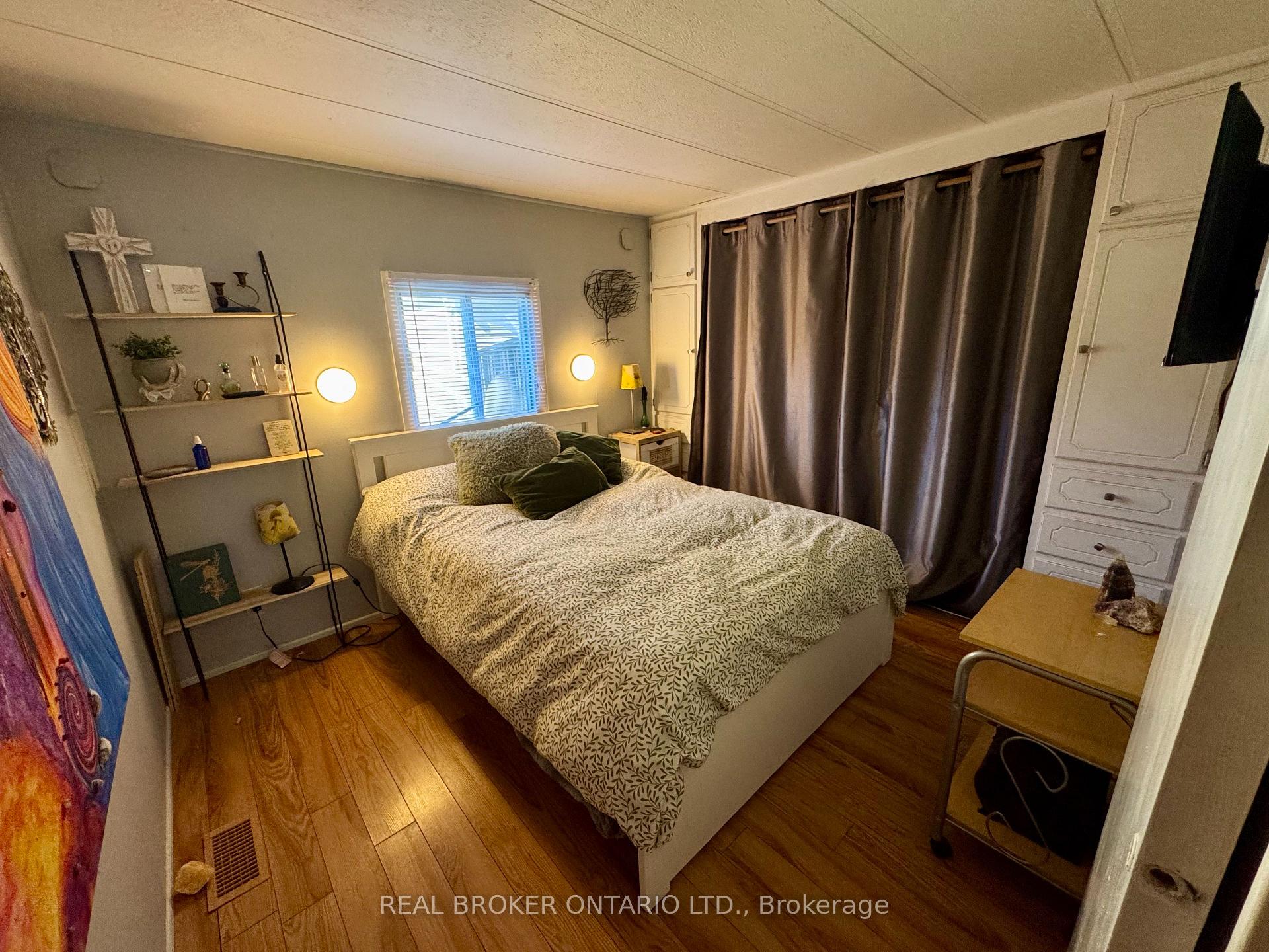 Furnished bedroom with a patterned bedspread, dark curtains, and wood flooring.