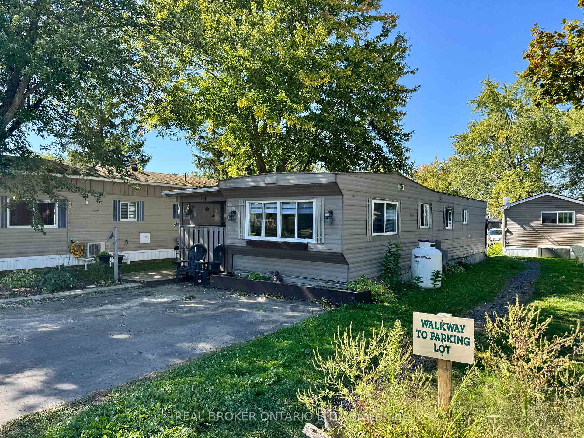 Gray manufactured home with a covered porch beside a sign directing visitors to the parking lot.
