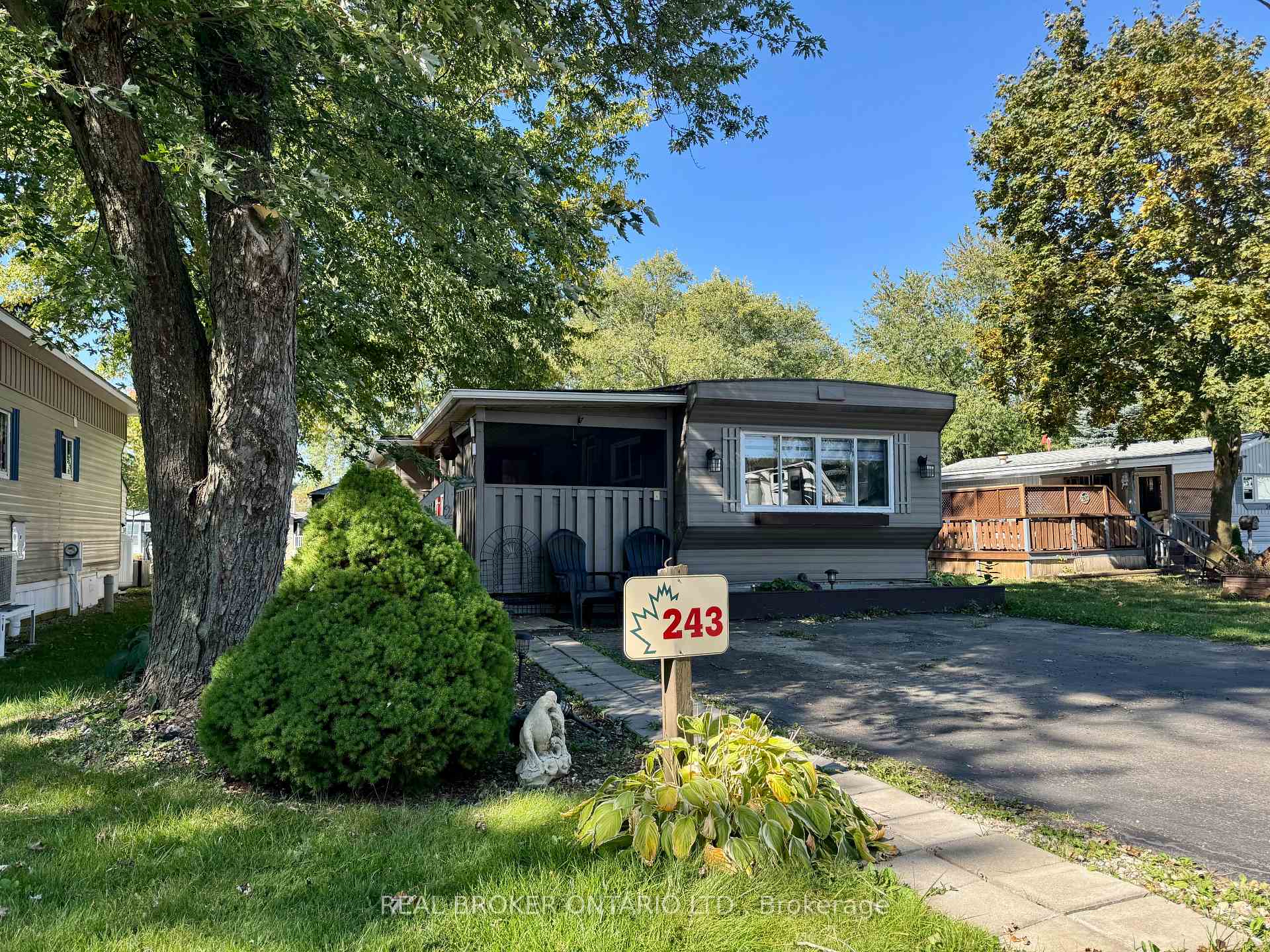 Gray home with a screened porch and front sign marked 243, beneath mature trees.