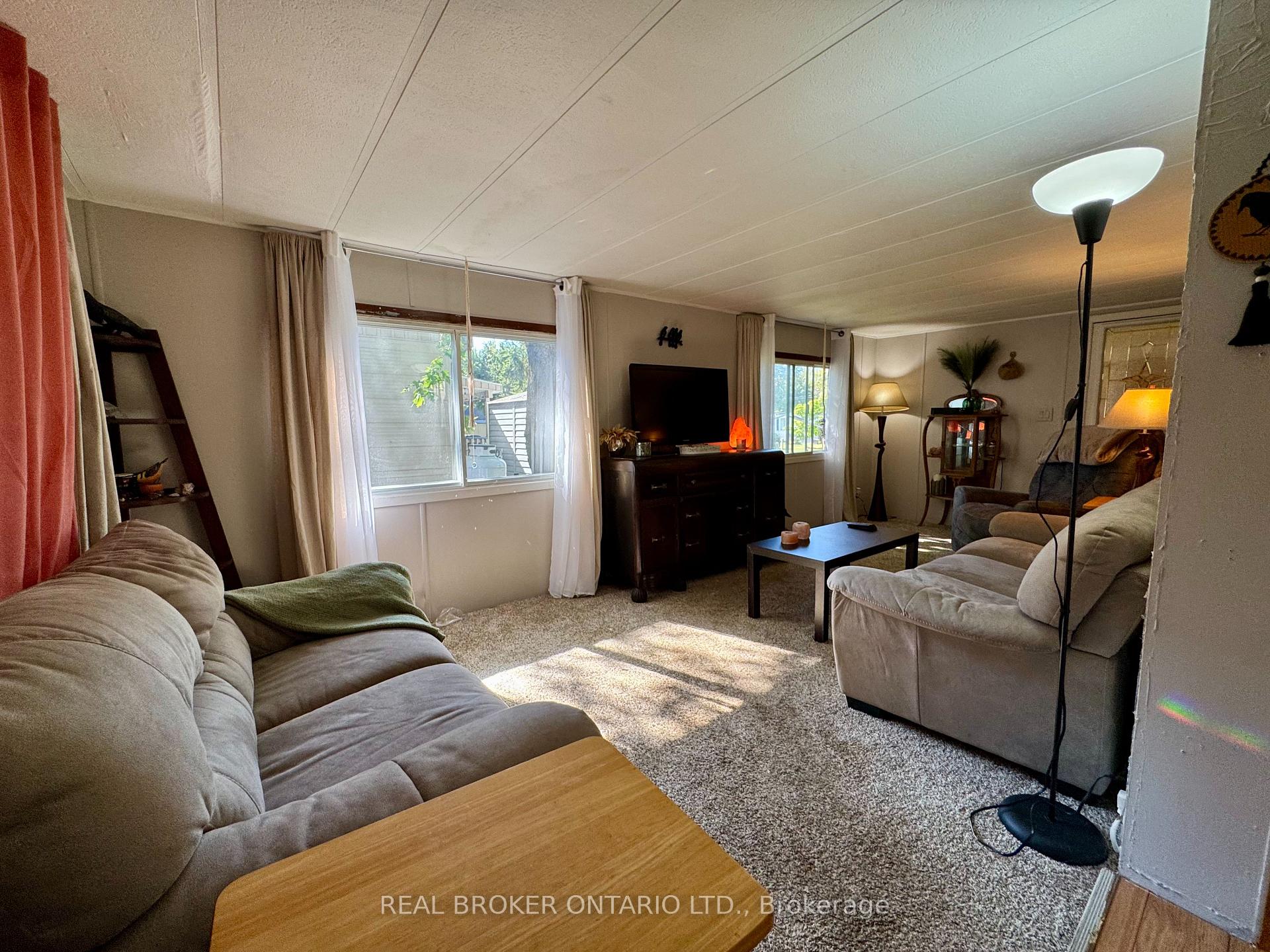Living room with beige sofas, a TV cabinet, and sunlight streaming through the windows.