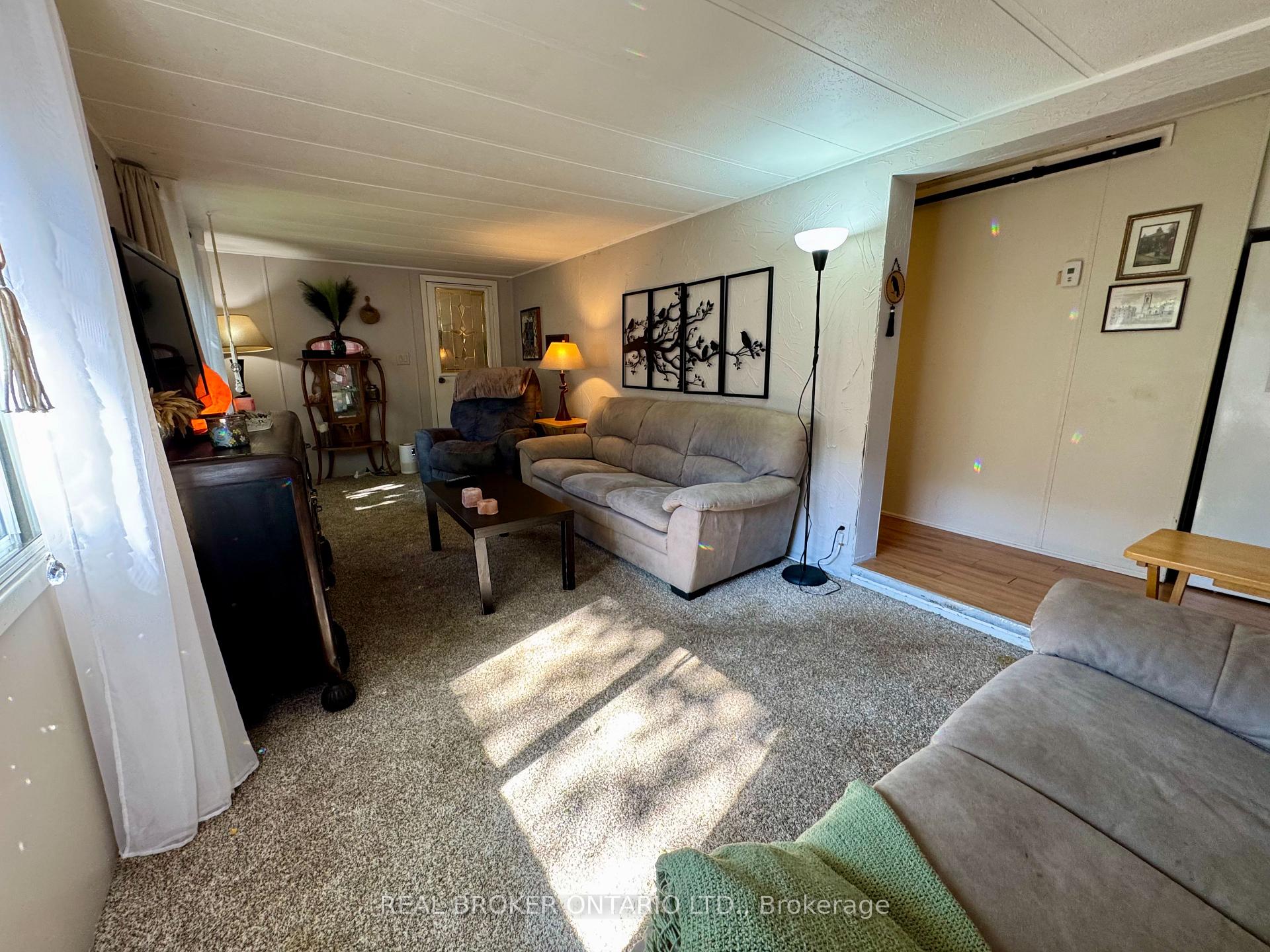 Living room with gray sofas, carpeted flooring, and sunlight streaming across the room.