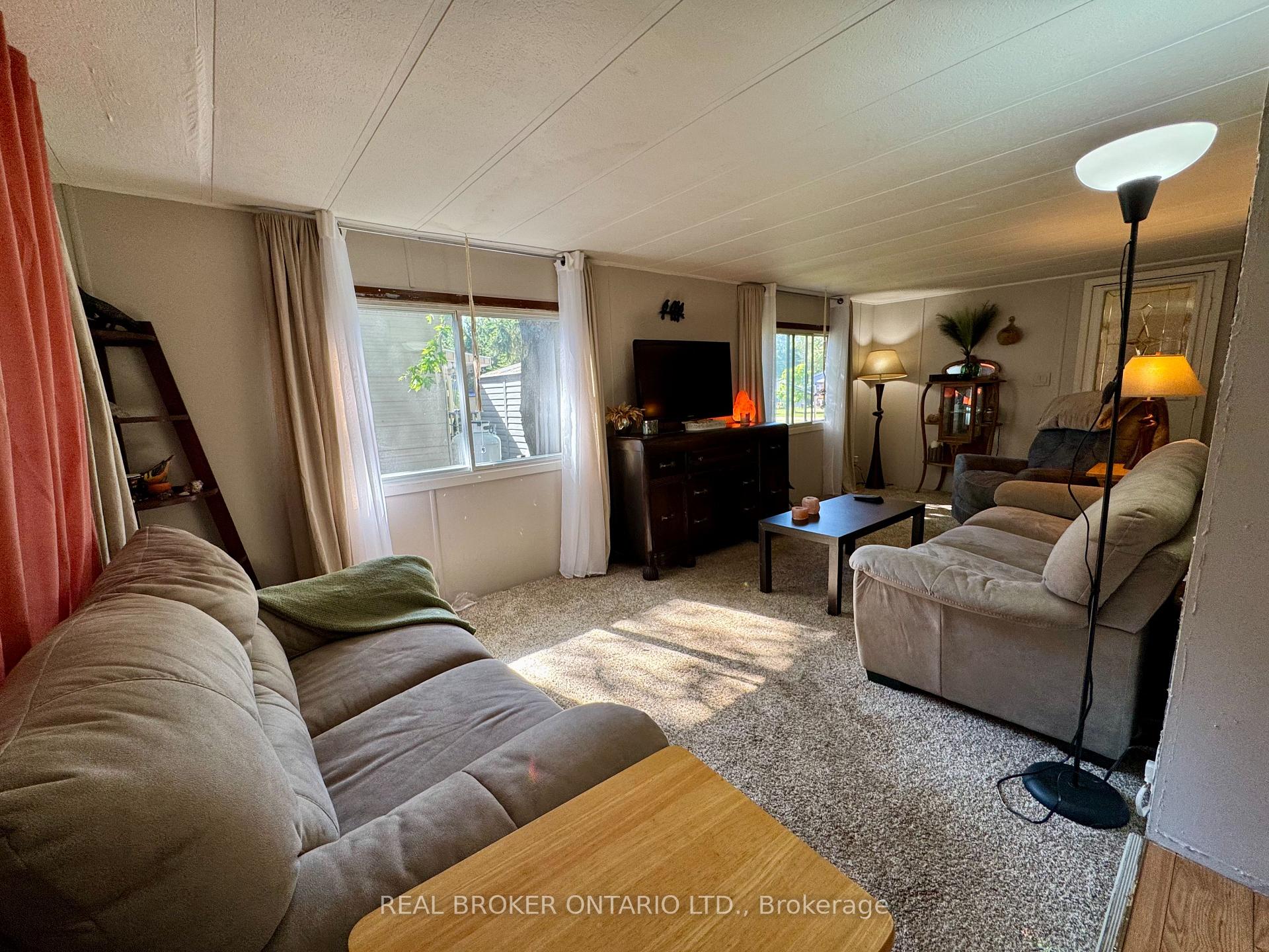 Furnished living room with beige sofas, carpet, and large windows beside a television.