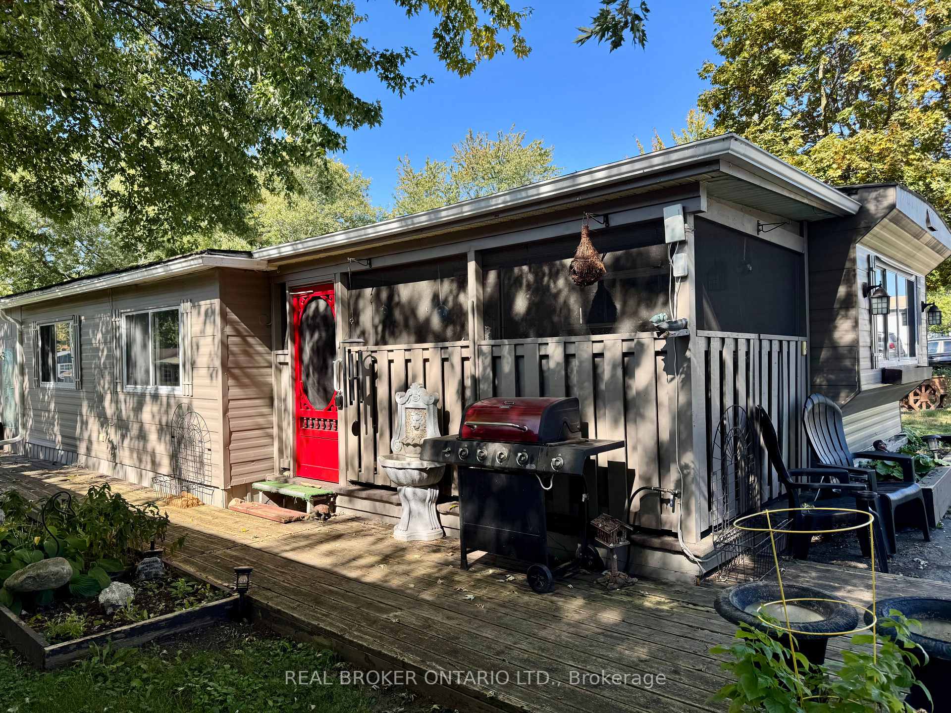 Gray home with a wooden deck, red entry door, barbecue grill, and garden beds.