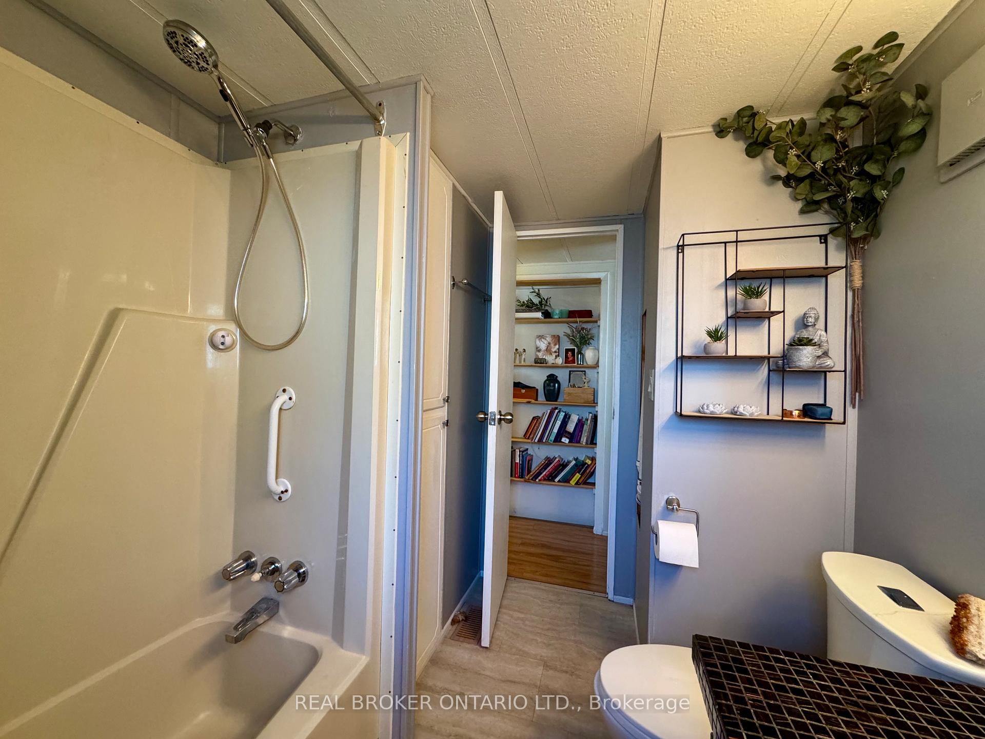 Bathroom with a grab bar beside the tub and decorative shelving above the toilet.