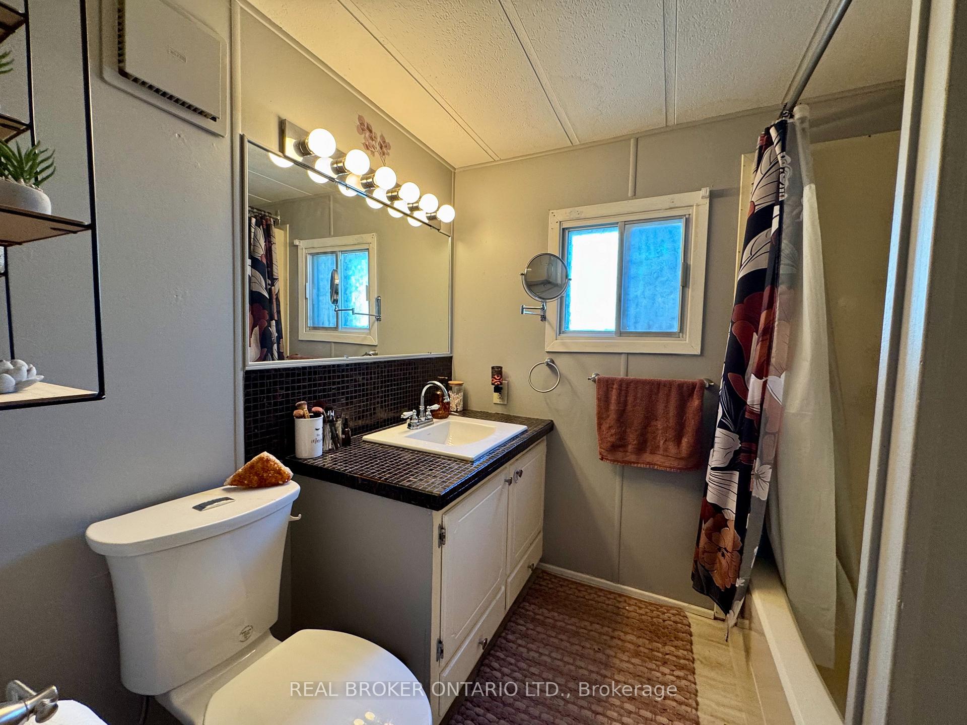 Bathroom with a black-tiled vanity, large mirror, window, and patterned shower curtain.