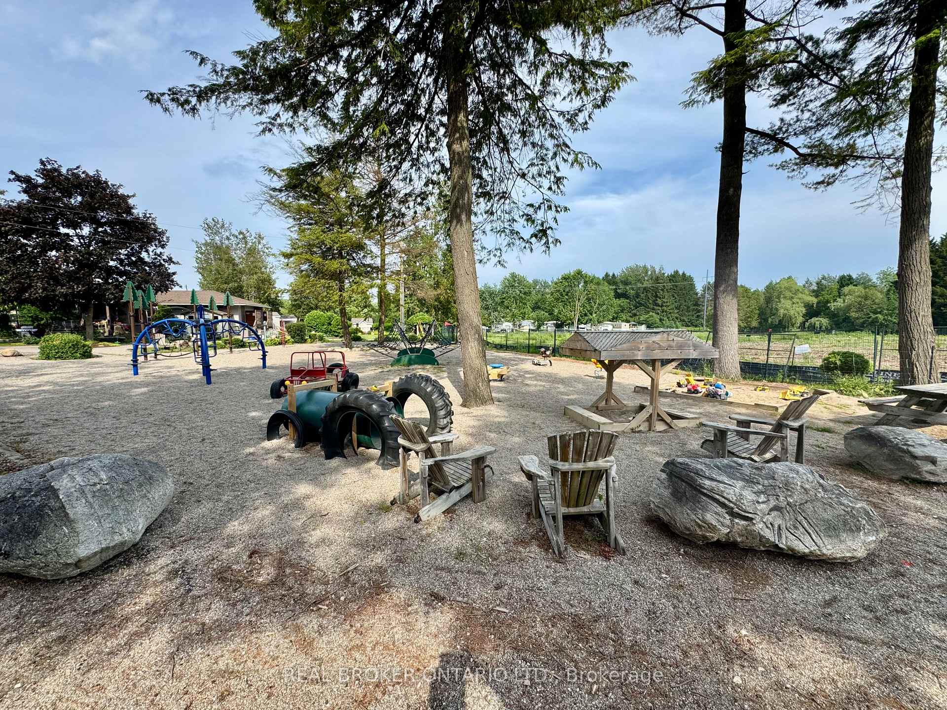 Outdoor playground with climbing equipment, tire tunnels, and wooden seating beneath mature trees.