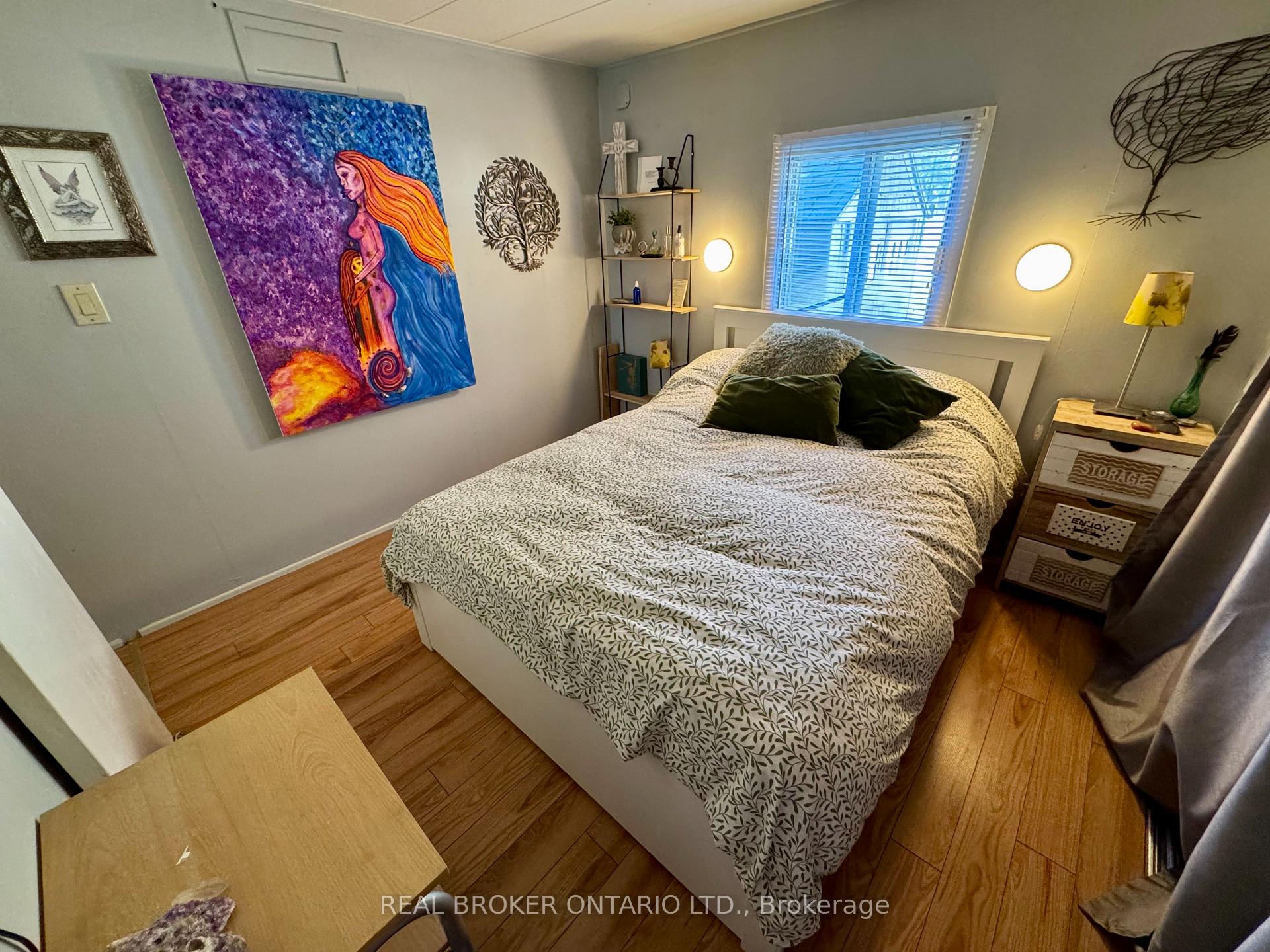 Furnished bedroom with a leafy-patterned bedspread, colorful wall art, and warm wood flooring.