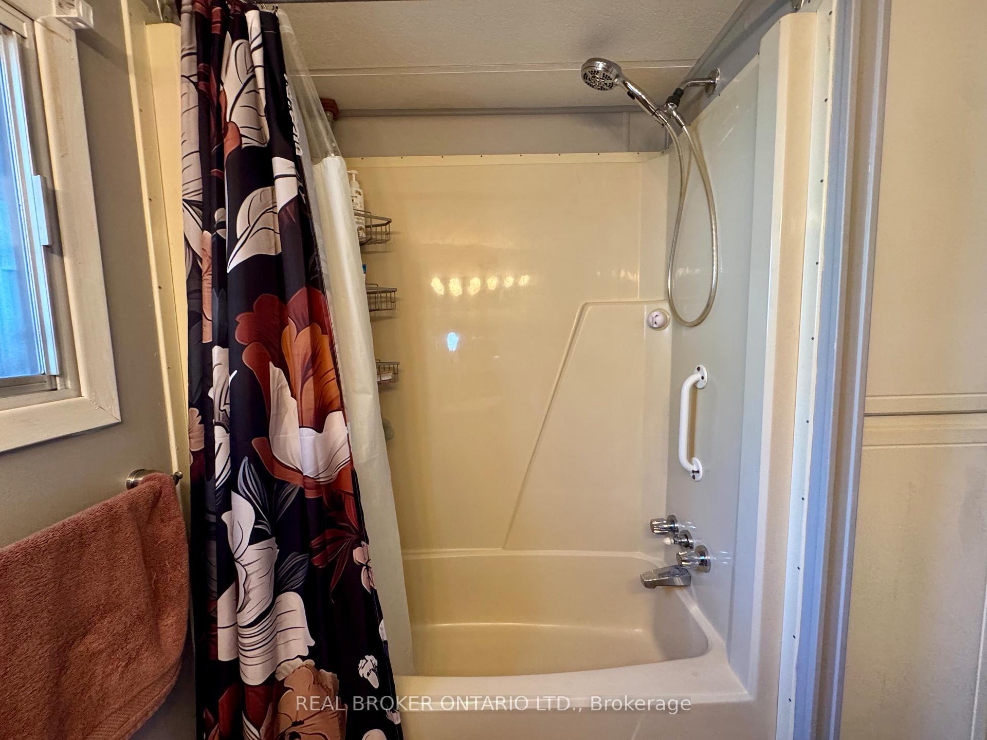 Bathroom tub and shower with a grab bar, handheld showerhead, and floral curtain.