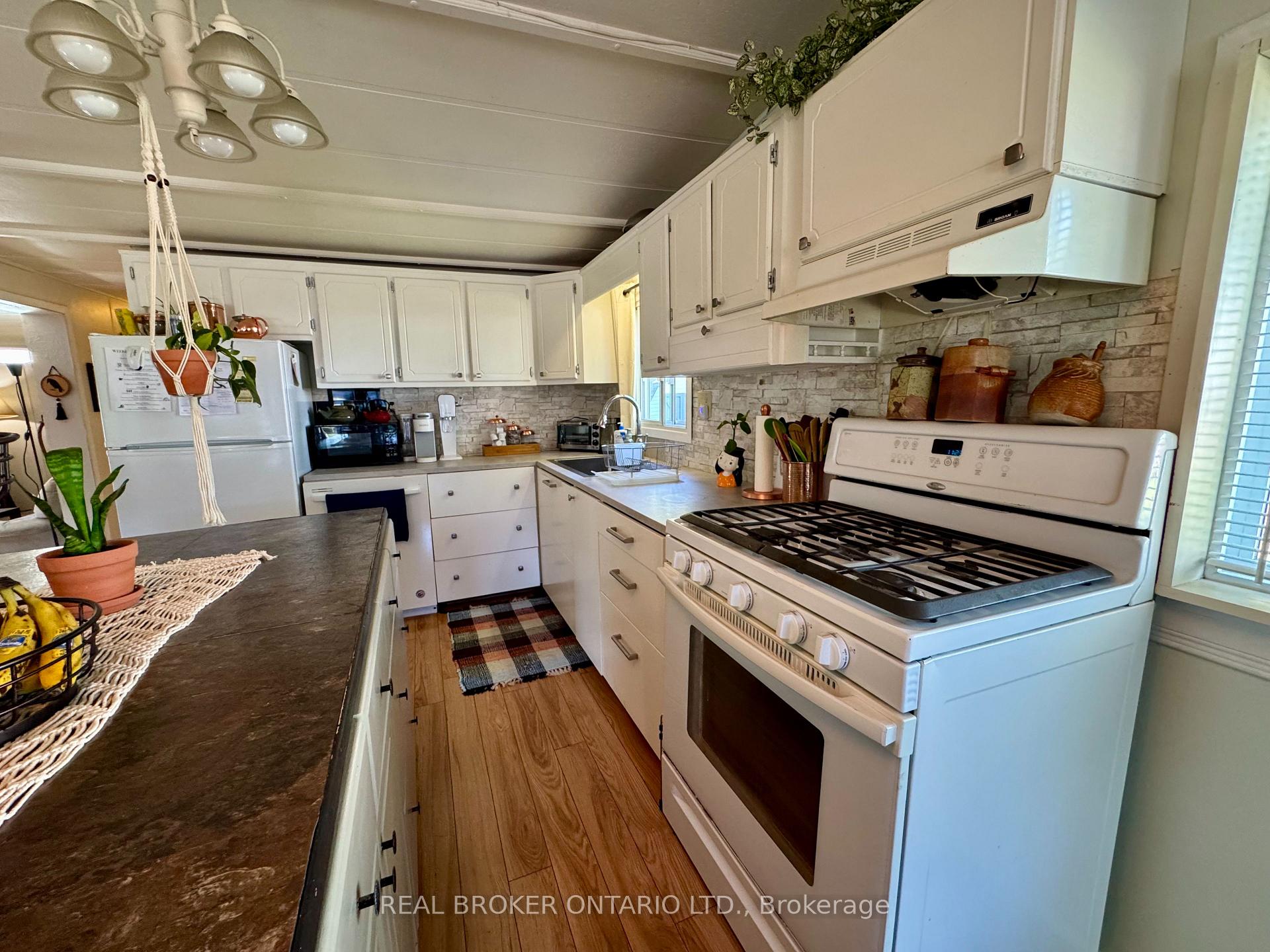Kitchen with white cabinets, gas range, stone-pattern backsplash, and dark island countertop.