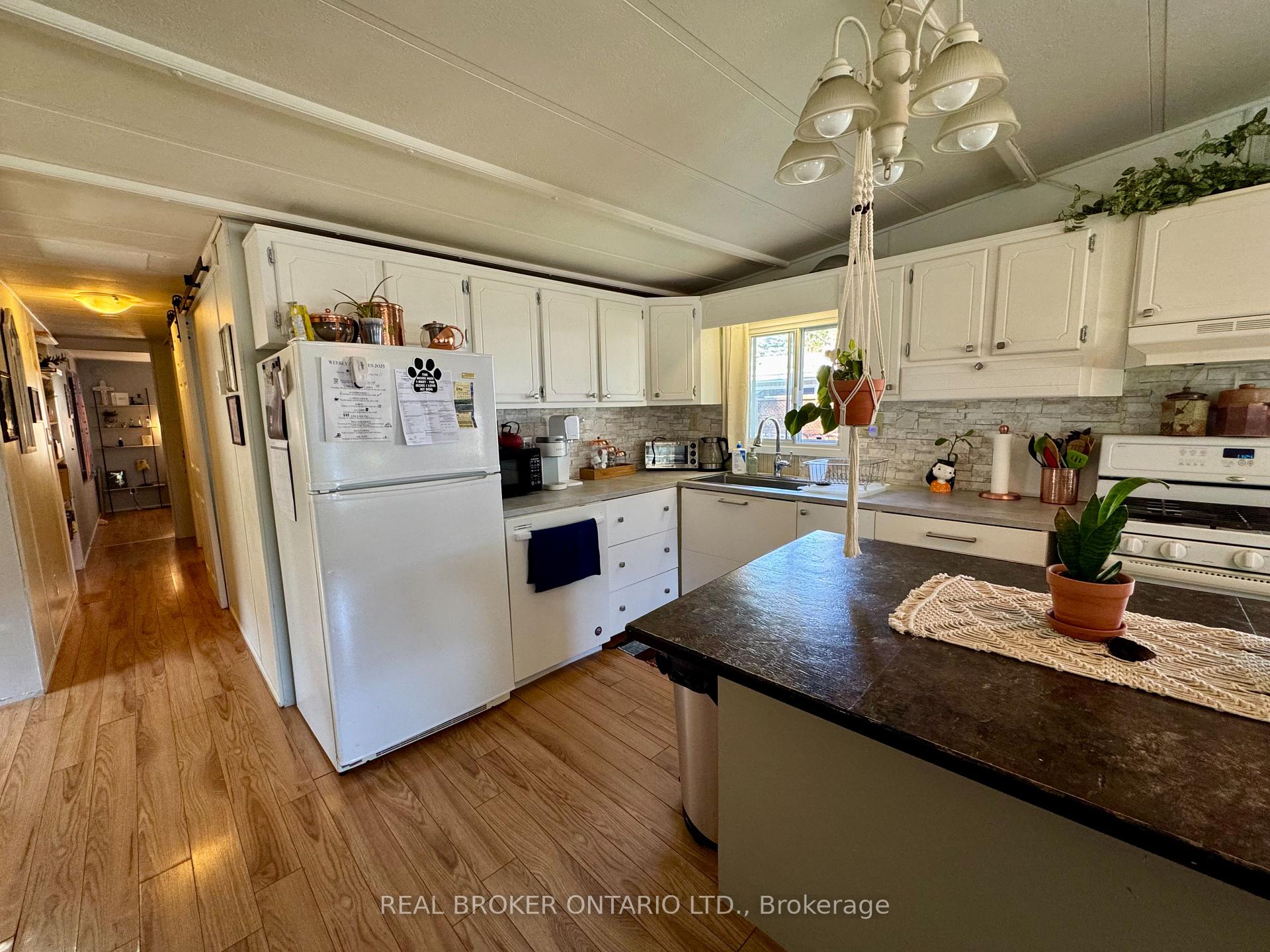 Kitchen with white cabinets, stone backsplash, dark island countertop, and a hanging plant.