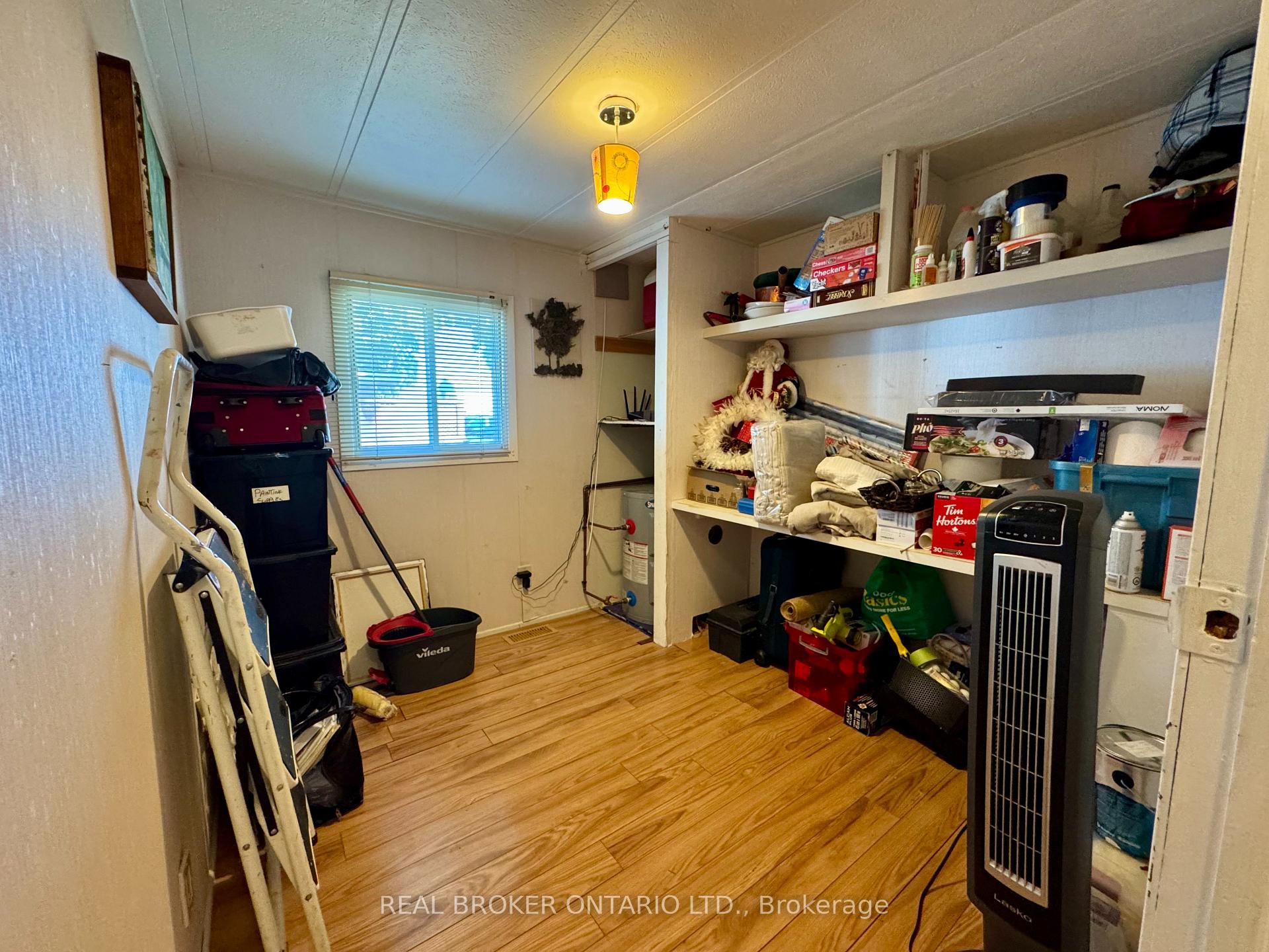 Storage room with packed shelves, stacked bins, cleaning supplies, and wood-look flooring.