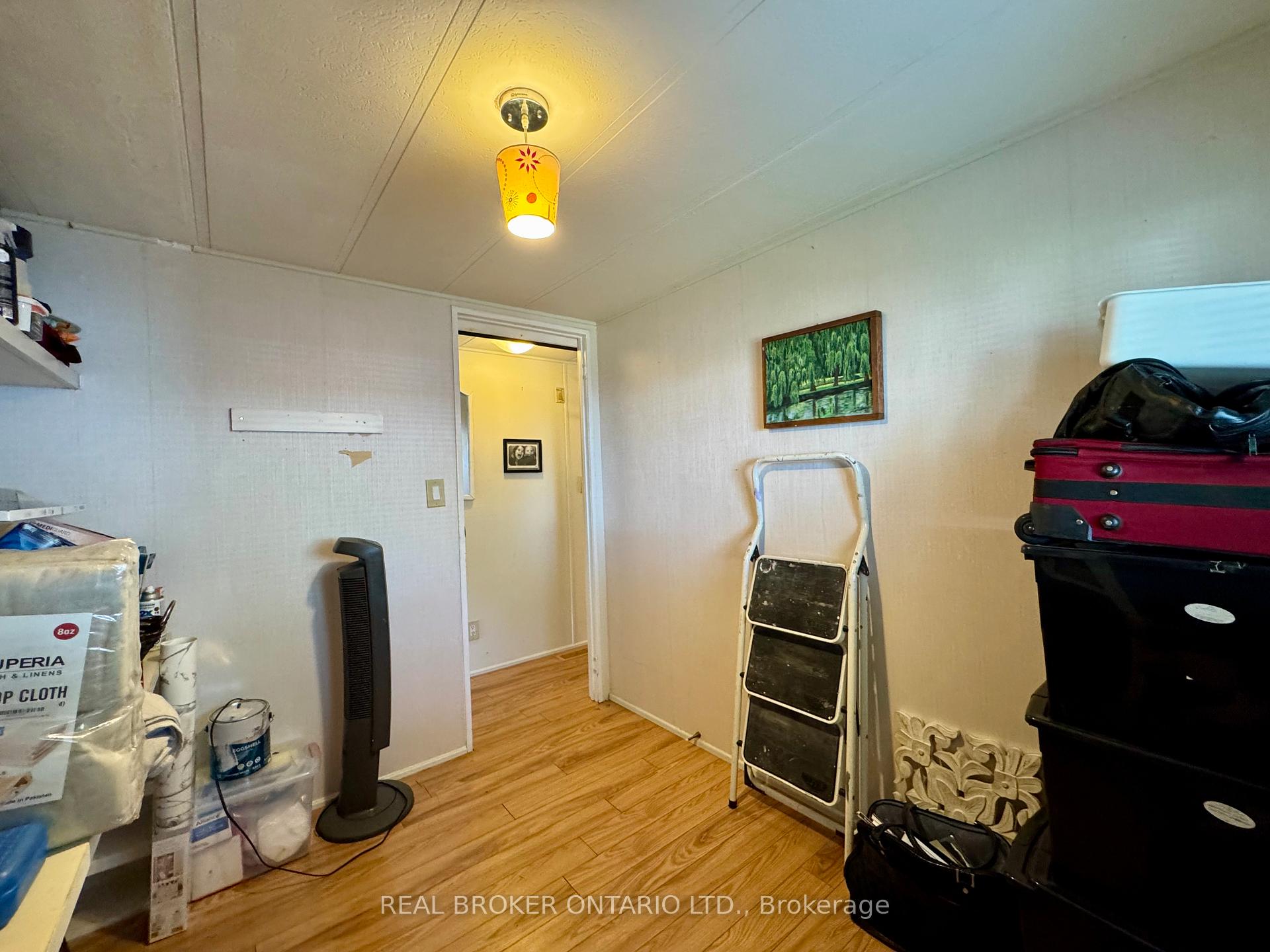 Cluttered storage room with wood-look flooring, a yellow pendant light, stacked luggage, and a folding ladder.