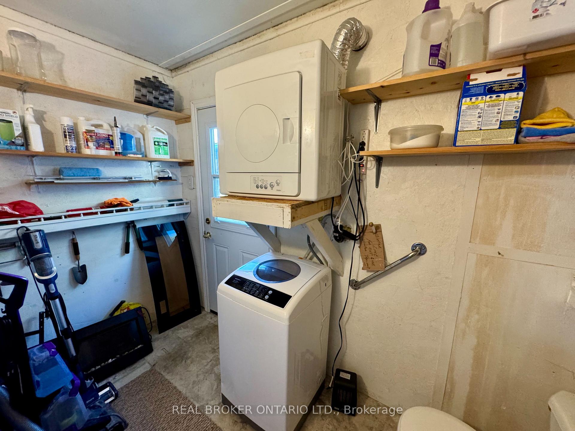 Laundry room with a top-loading washer, wall-mounted dryer, and shelves of cleaning supplies.