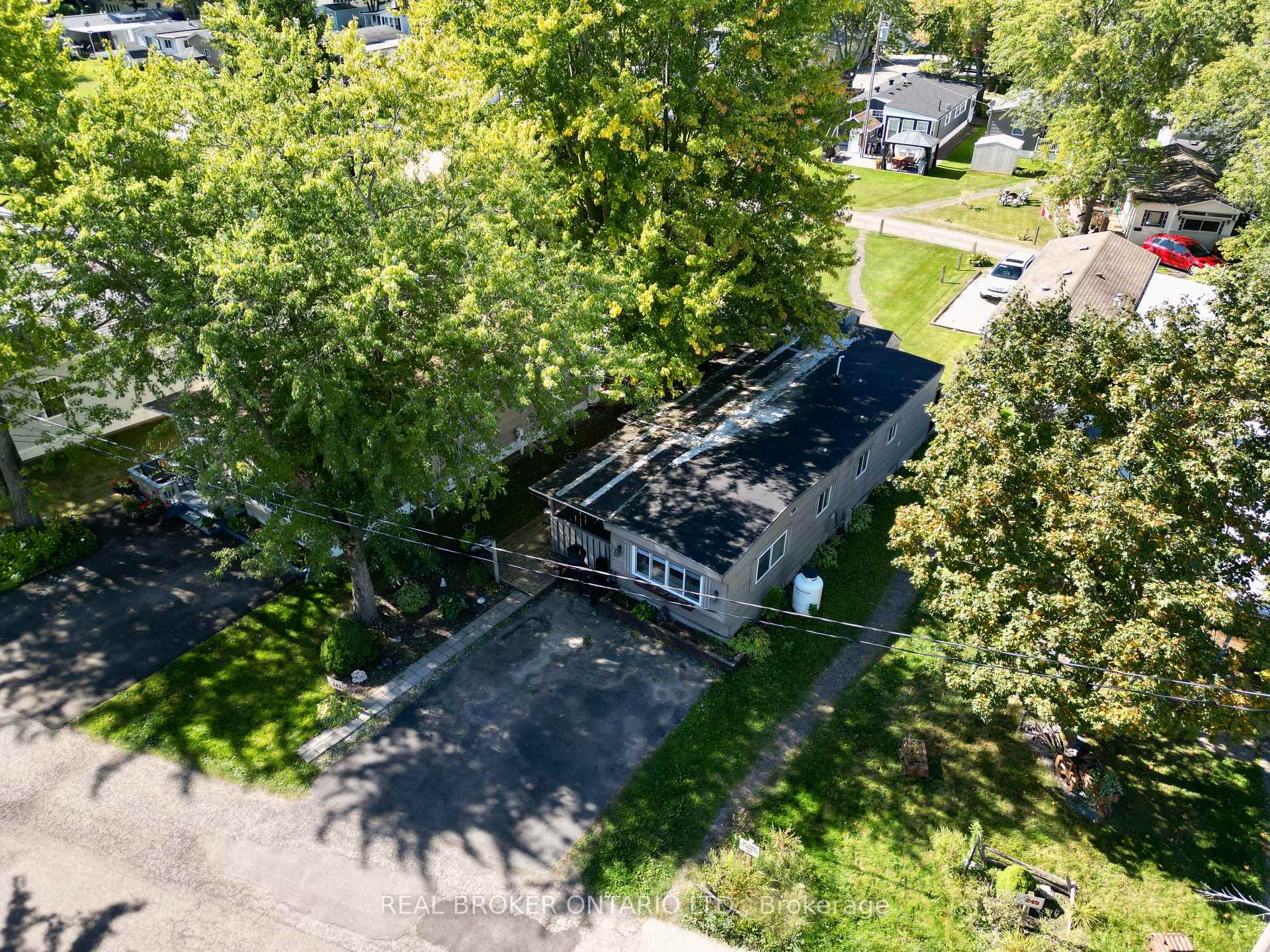 Aerial view of a single-story home surrounded by mature trees, with a paved driveway and neighboring homes.