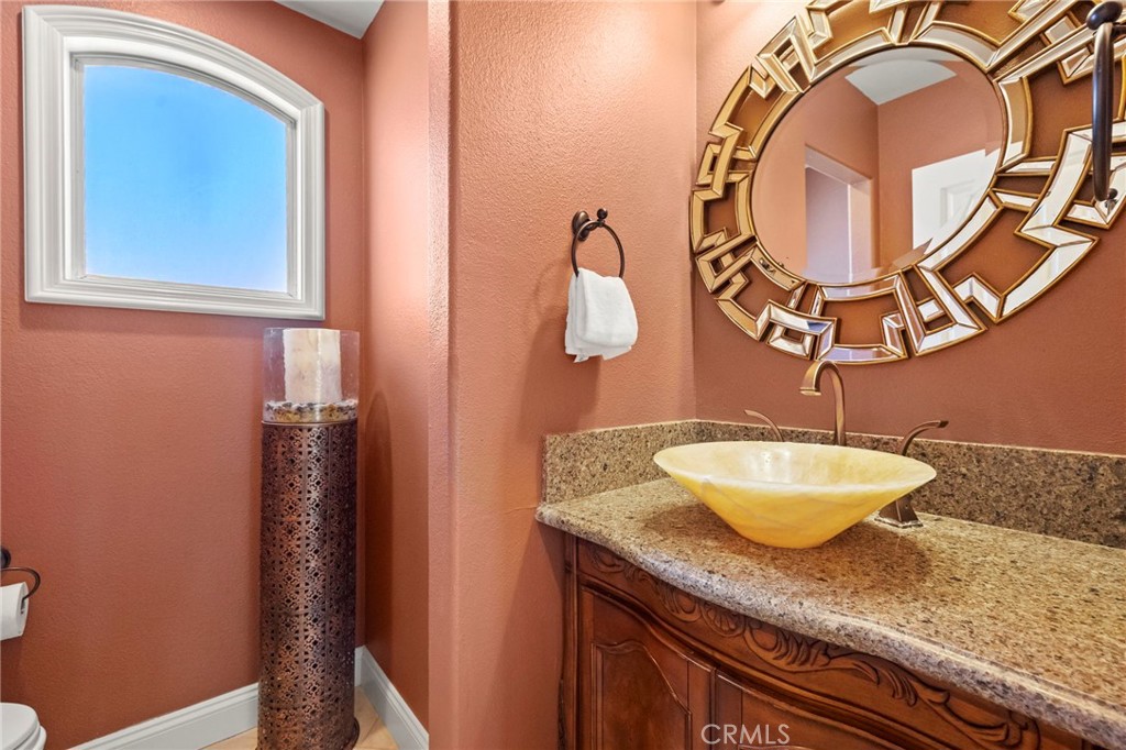Powder room with a vessel sink, granite counter, carved wood vanity, and ornate mirror.