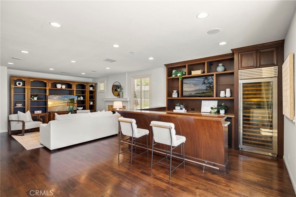 Entertainment room with built-in shelving, white seating, and a curved bar beside a glass-front wine refrigerator.