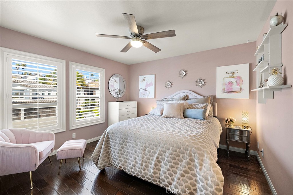 Bedroom with a patterned quilt, pink walls, shuttered windows, and a ceiling fan.