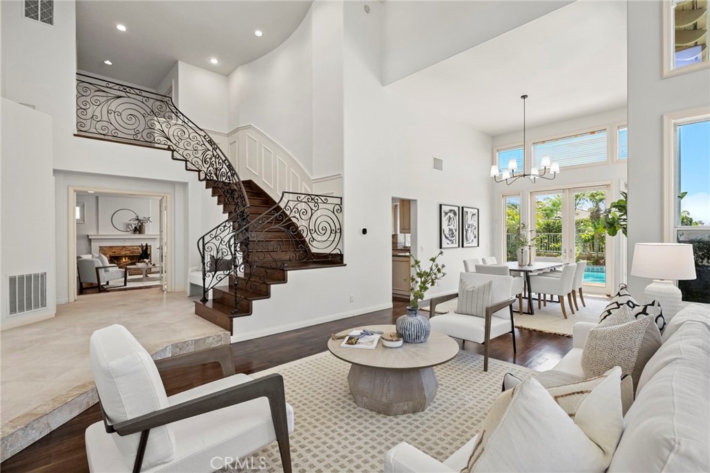 Living room with a curved staircase, ornate iron railing, and dining area overlooking a pool.