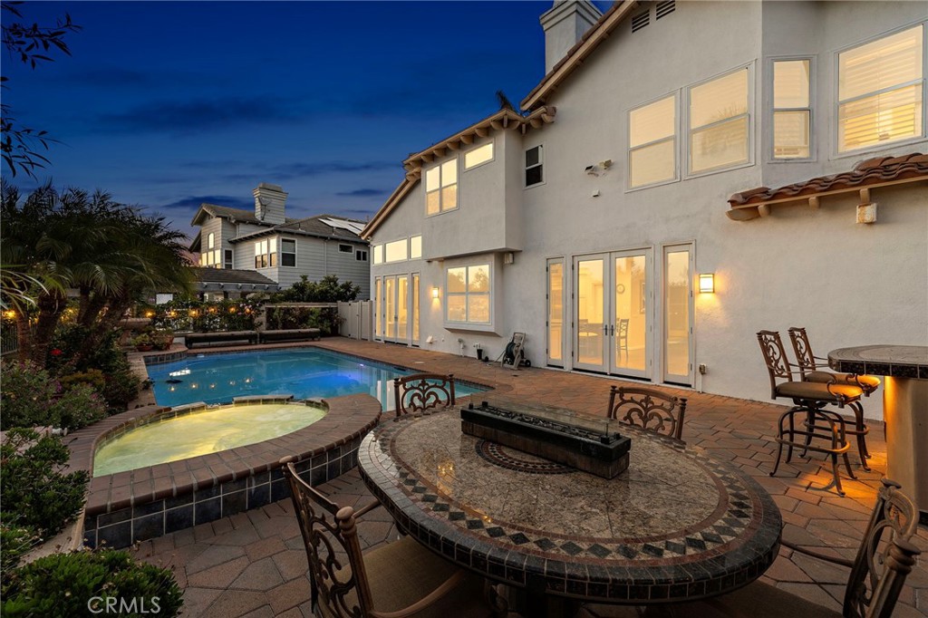 Backyard pool and raised spa beside a tiled patio with an outdoor fireplace at dusk.