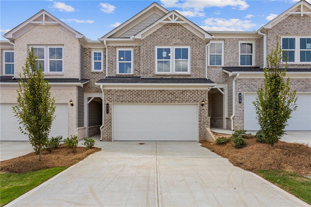 Brick townhouse with a wide driveway, attached garage, and neighboring homes.