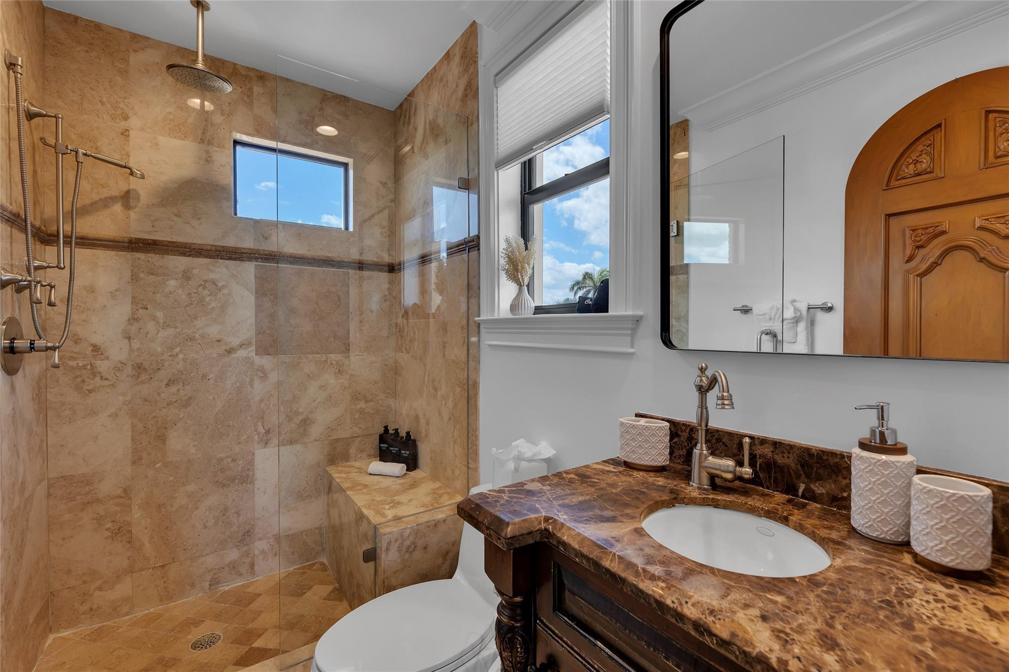 Bathroom with a tan stone walk-in shower, built-in bench, and dark marble vanity.