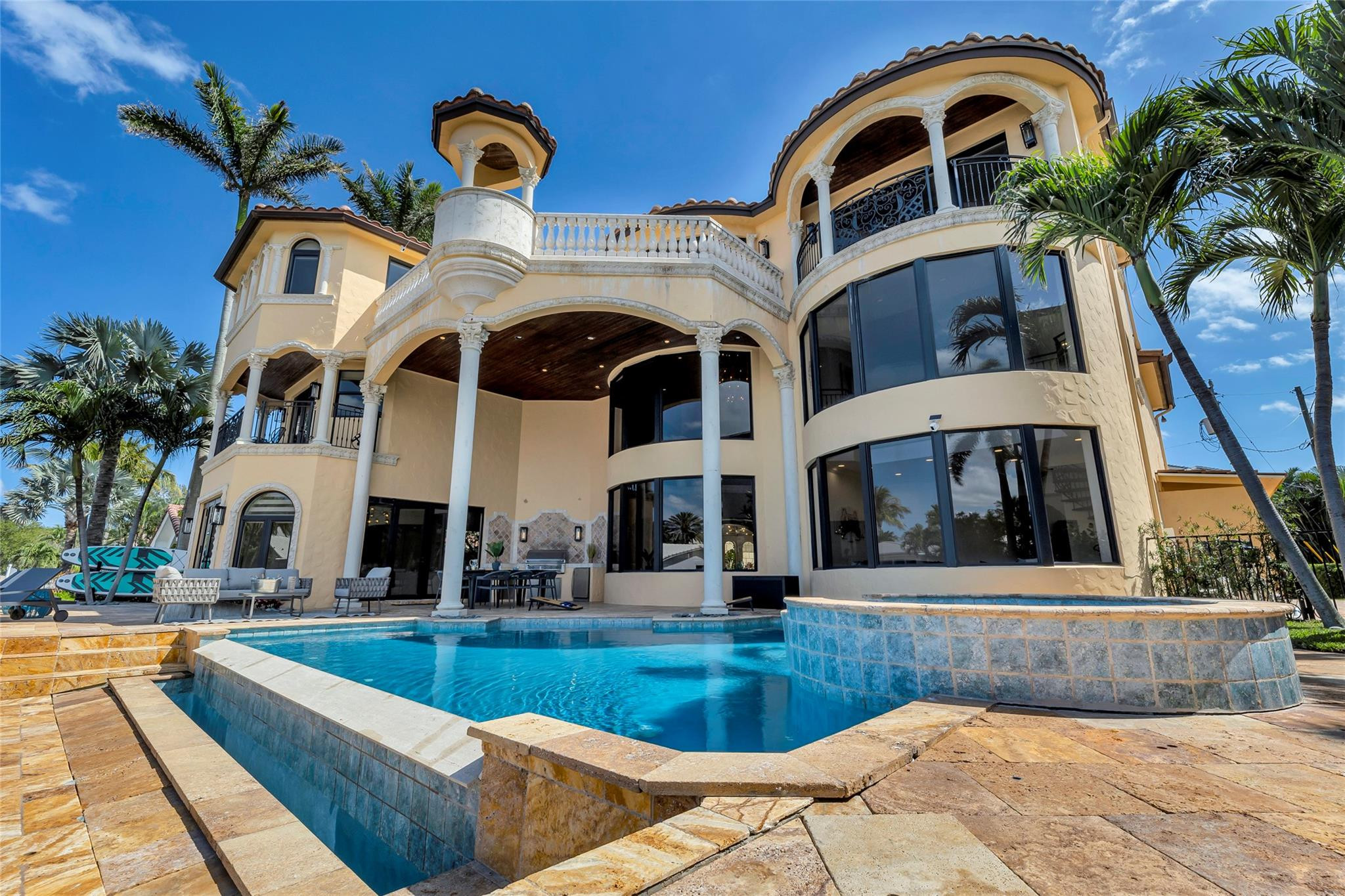 Mediterranean-style home with arched balconies and columns behind a pool and raised circular spa.