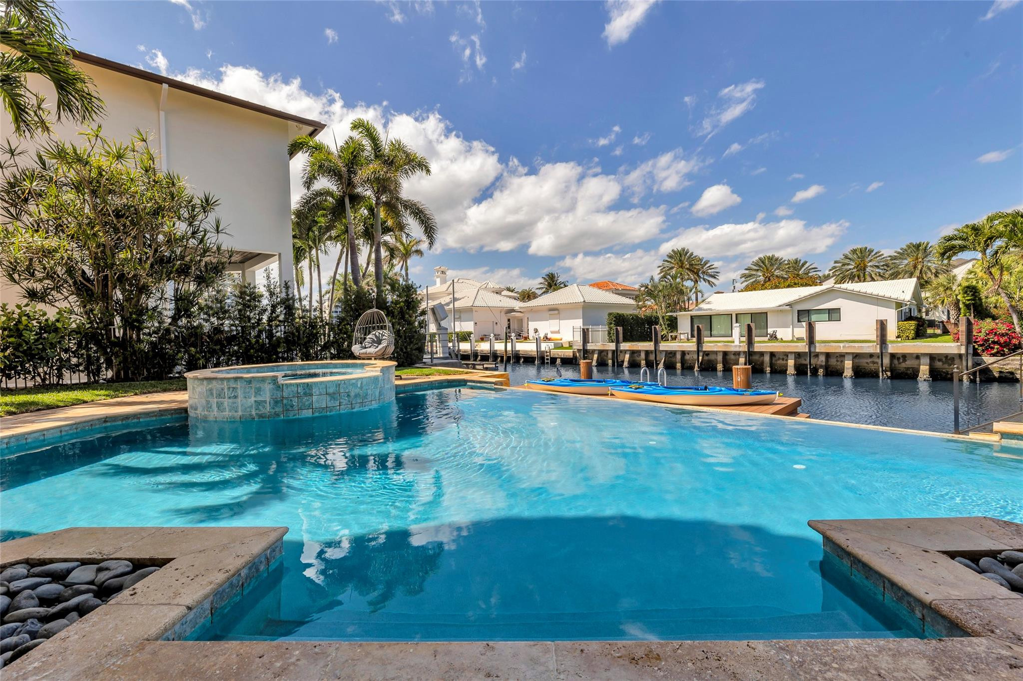 Backyard pool and raised spa overlook a canal, with kayaks and palm-lined homes across the water.