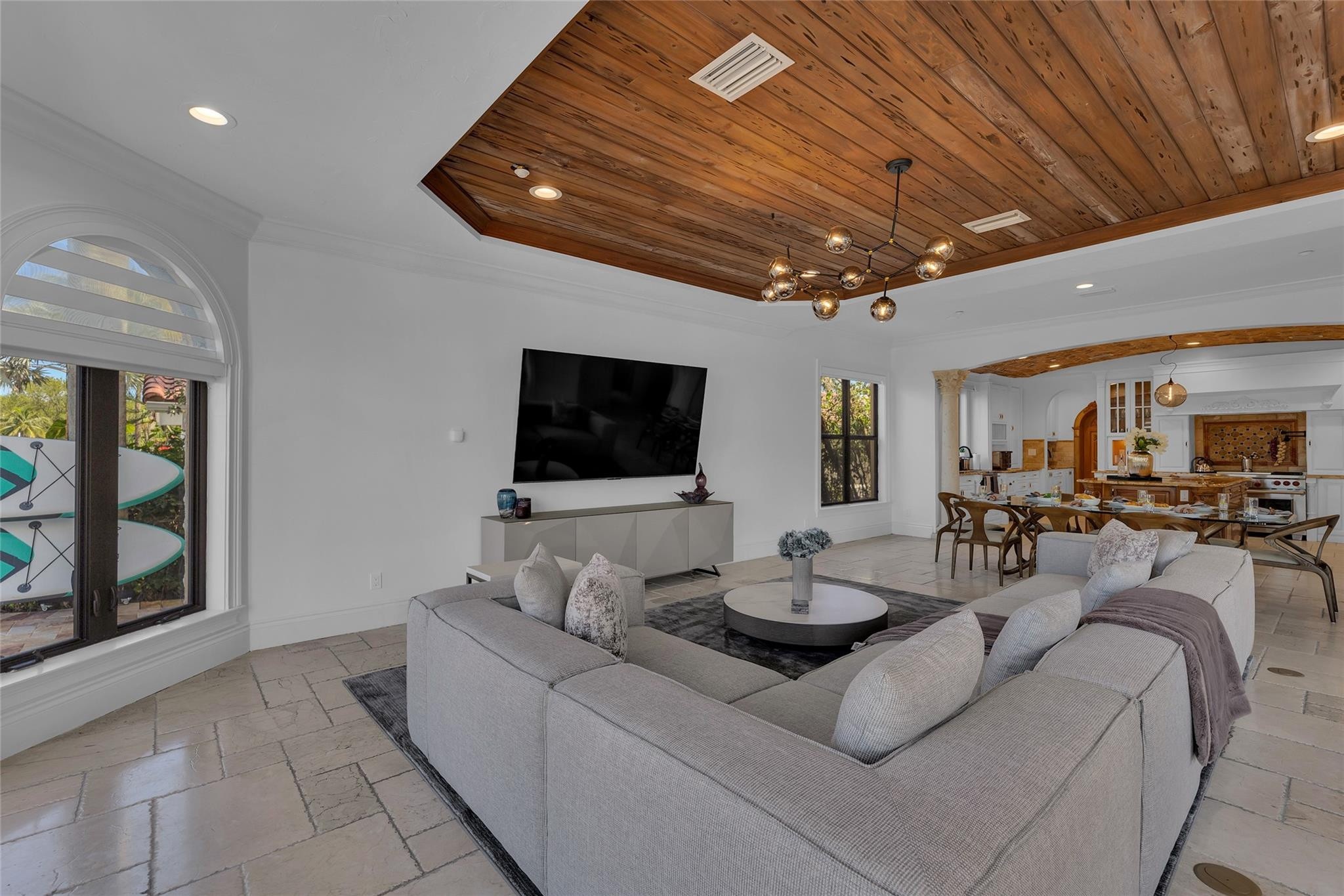 Living room with a wood-plank ceiling, gray sectional, and open dining area and kitchen.